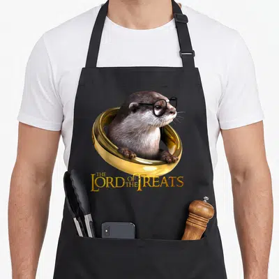 Tablier de cuisine noir avec une loutre portant des lunettes noires assise dans une grande anne dorée brillante.