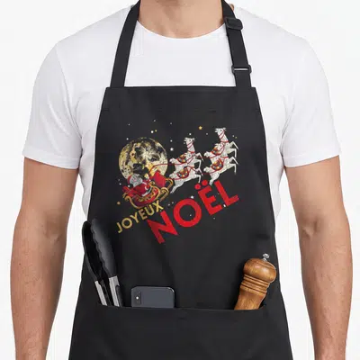 Tablier de cuisine noir avec illustration colorée d'un traîneau de Père Noël et l'inscription Joyeux Noël en lettres rouges et dorées.