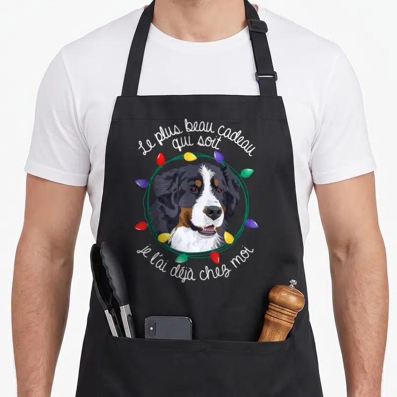 Tablier de cuisine noir avec un portrait de bouvier bernois encadré par des lumières de Noël colorées et du texte blanc.
