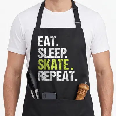 Tablier de cuisine noir avec inscription Eat Sleep Skate Repeat en blanc et vert lime, style typographie usée.