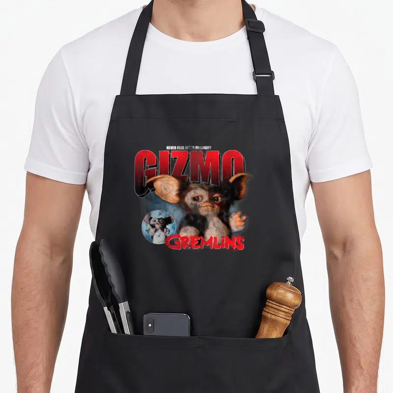 Tablier de cuisine noir avec une illustration de Gizmo et le texte Gremlins en rouge.