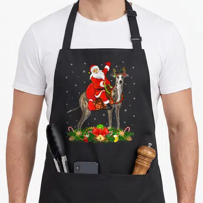 Tablier de cuisine noir avec illustration d'un Père Santa sur un Greyhound orné de guirlandes et de décorations de Noël.