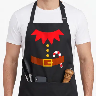 Tablier de cuisine noir avec illustration de costume de lutin rouge, ceinture marron et canne à sucre blanche et rouge.