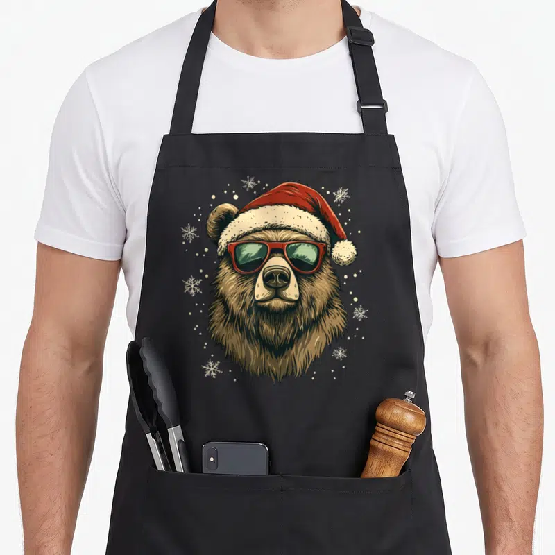 Tablier de cuisine noir avec illustration d'un ours grizzly au chapeau de Père Noël et lunettes de soleil rouges.