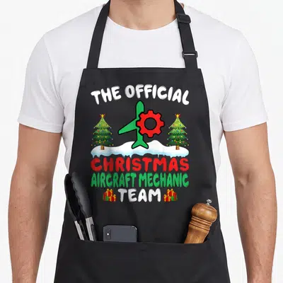 Tablier de cuisine noir avec illustration d'avion vert, roue rouge et arbres de Noël sur neige.