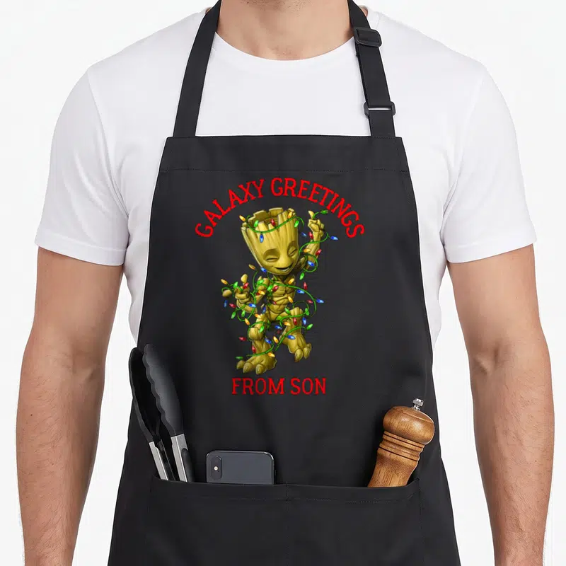 Tablier de cuisine noir avec Groot enroulé dans des guirlandes lumineuses et texte rouge.