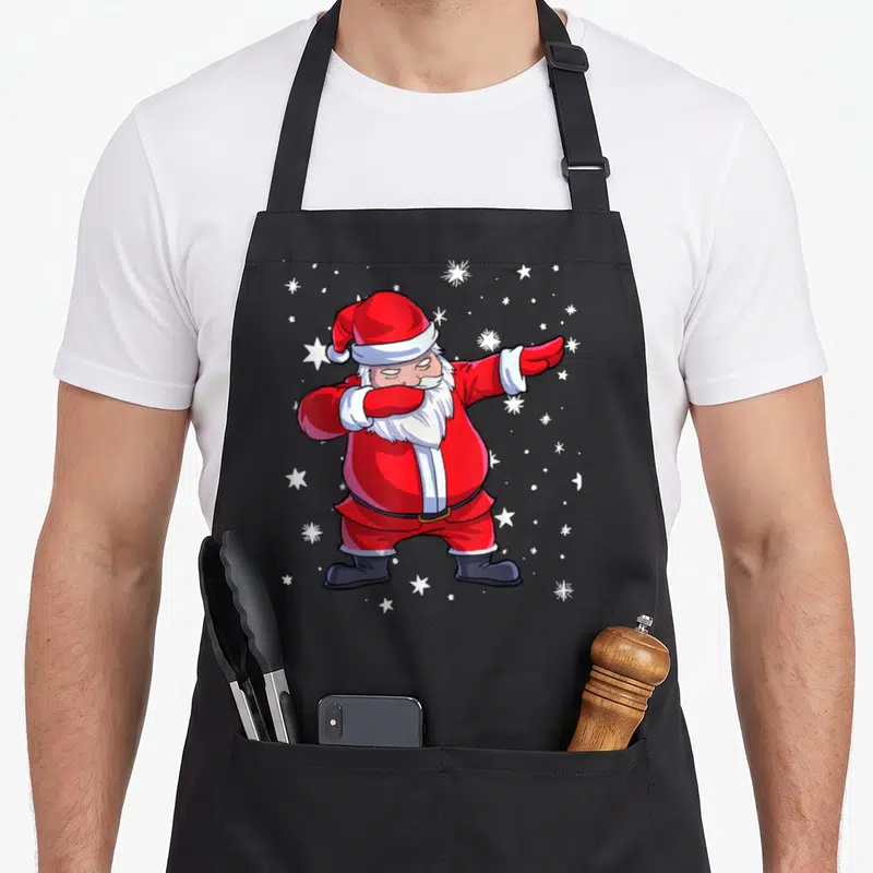 Tablier de cuisine noir avec un Père Noel en train de faire le dabbing entouré d'étoiles blanches.