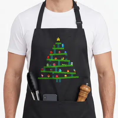 Tablier de cuisine noir avec sapin de Noël formé de plateformes vertes et de personnages pixelisés colorés.
