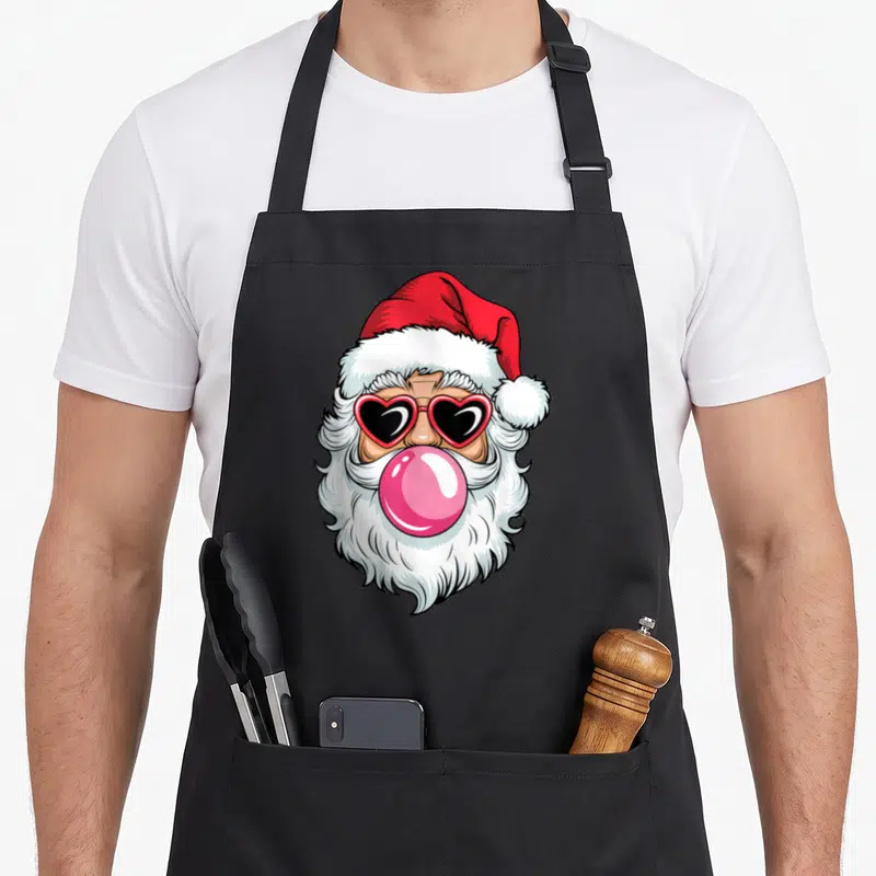 Tablier de cuisine noir avec illustration d'un Père Santa cool aux lunettes cœur et une bulle de gomme rose.