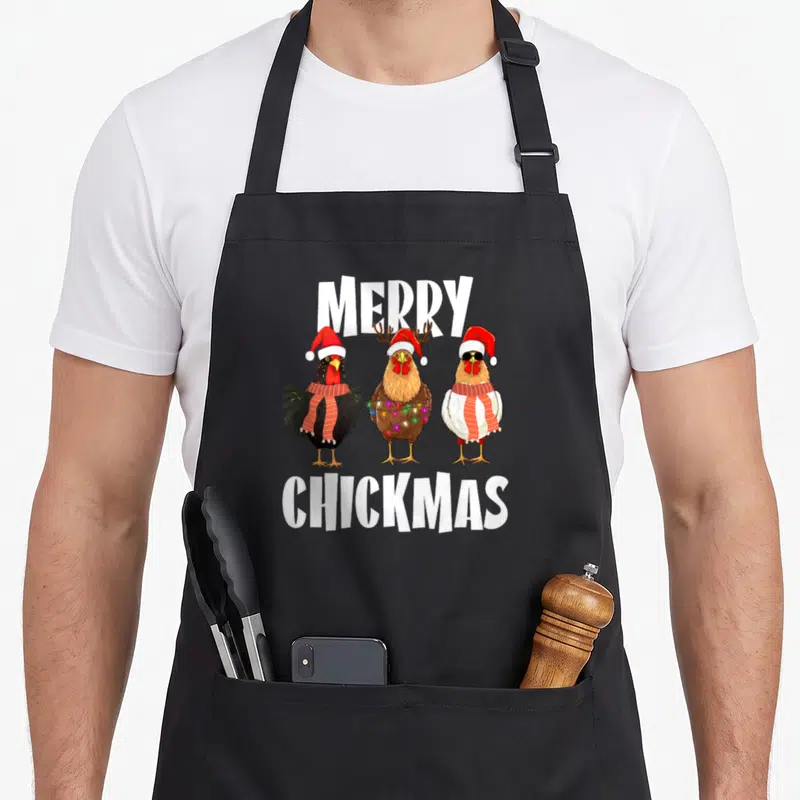 Tablier de cuisine noir avec trois poules portant des chapeaux de Père Noël et des écharpes sous le texte Merry Chickmas.