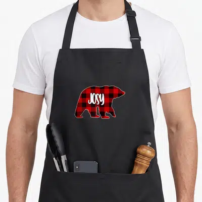 Tablier de cuisine noir avec un ours aux carreaux rouges et le prénom Josy en blanc.
