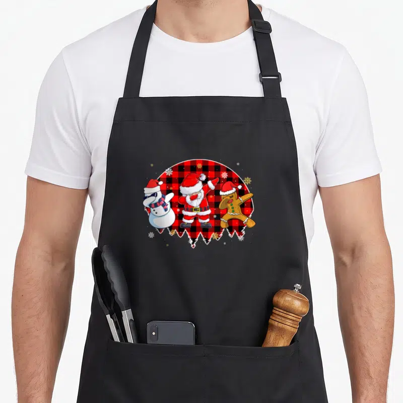 Tablier de cuisine noir avec Père Noël, bonhomme de neige et biscuit en train de faire le dab sur fond tartan.
