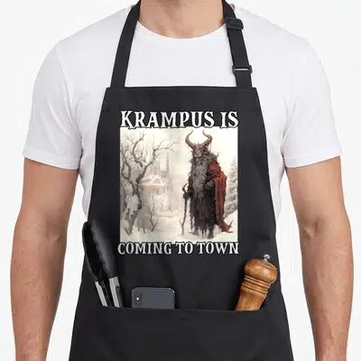 Tablier de cuisine noir avec illustration de Krampus et texte « KRAMPUS IS COMING TO TOWN » sur fond hivernal.