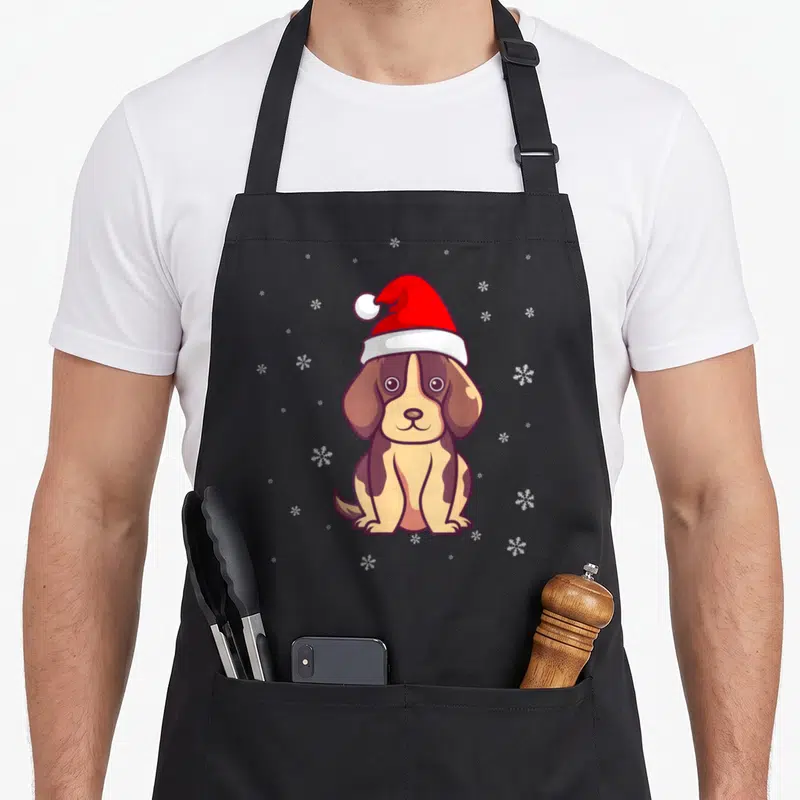 Tablier de cuisine noir avec illustration d'un chien marron portant un chapeau de Noël rouge et des flocons de neige blancs.