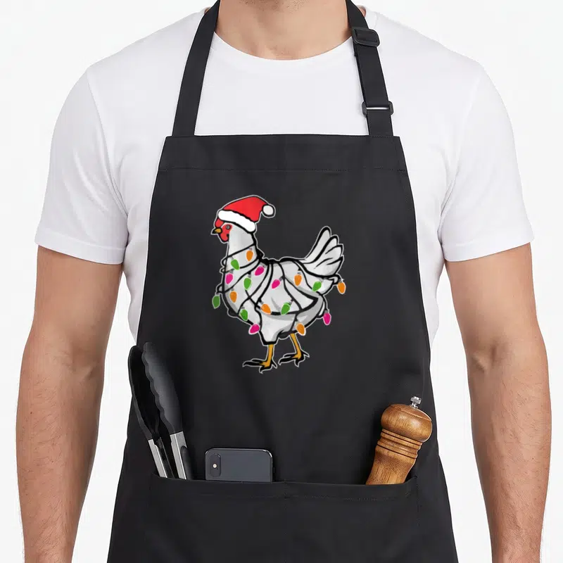 Tablier de cuisine noir avec illustration d'un poulet portant un bonnet de Père Noël et des lumières scintillantes.