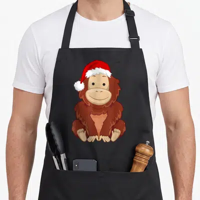 Tablier de cuisine noir avec illustration d'un orang-outan souriant coiffé d'un bonnet de Père Noël rouge et blanc.