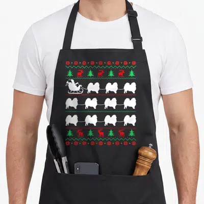 Tablier de cuisine noir avec motif de Pomeranians blancs tirant un traîneau de Père Noël sur fond gris uni.