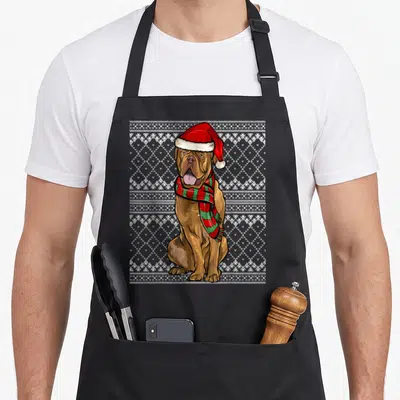 Tablier de cuisine noir avec illustration d'un chien marron portant un bonnet de Père Noël et une écharpe verte et rouge.