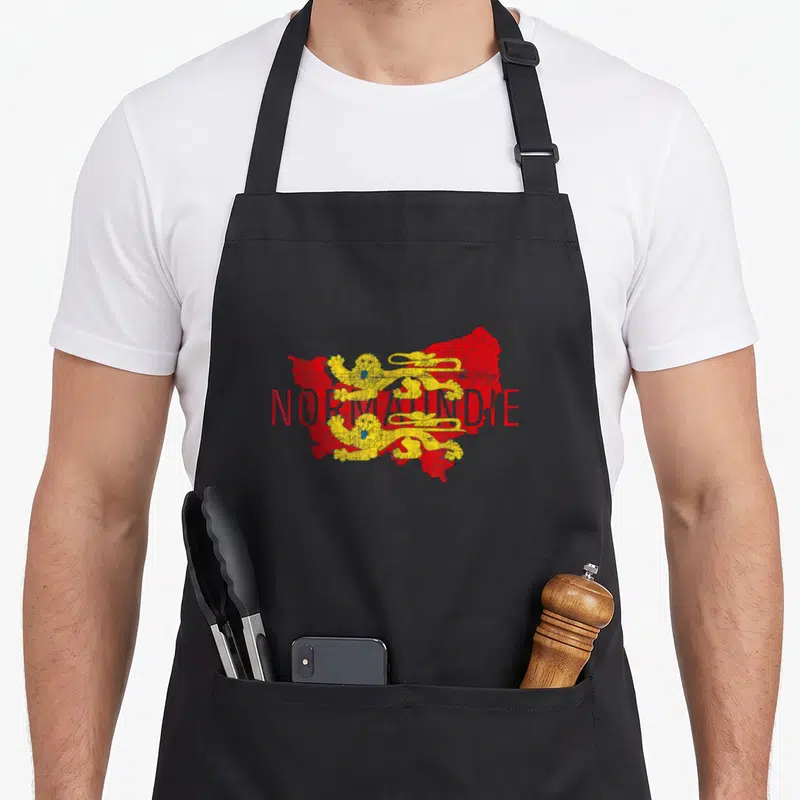 Tablier de cuisine noir avec carte rouge de Normandie et deux lions dorés superposés au texte NORMANDIE en rouge.