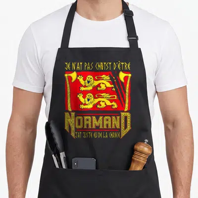 Tablier de cuisine noir avec inscription Je n'ai pas choisi d'être normand et deux lions jaunes sur fond rouge.