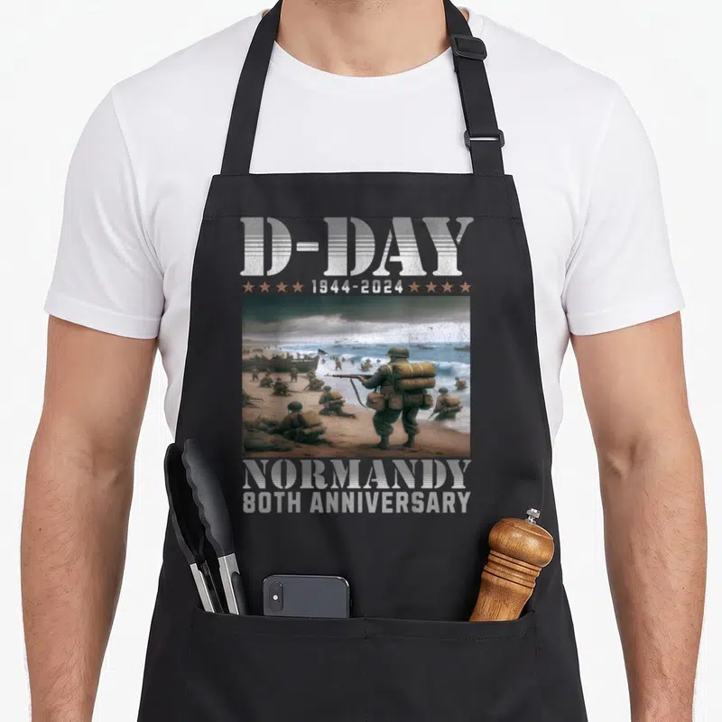 Tablier de cuisine noir avec illustration des débarquements D-Day et texte D-Day Normandy 80th Anniversary en typographie vintage.