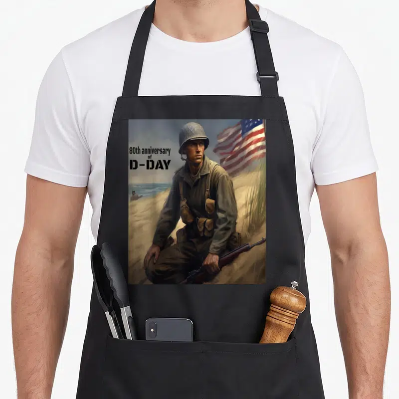 Tablier de cuisine noir avec illustration d'un soldat sur une plage et un drapeau américain en arrière-plan.