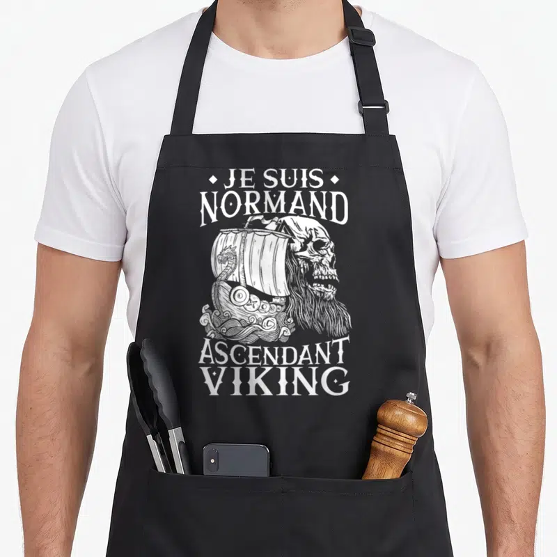 Tablier de cuisine noir avec illustration d'un crâne viking et d'un navire à voile blanc sur fond uni.