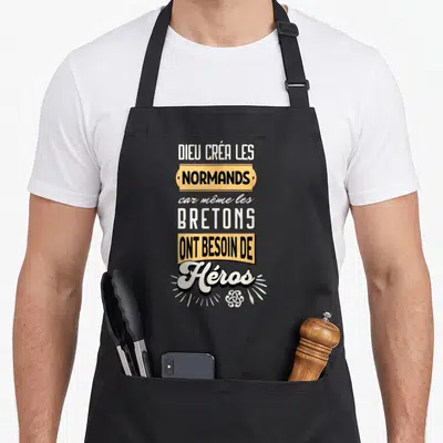 Tablier de cuisine noir avec typographie humoristique citant les Normands et les Bretons en lettres blanches et orange.