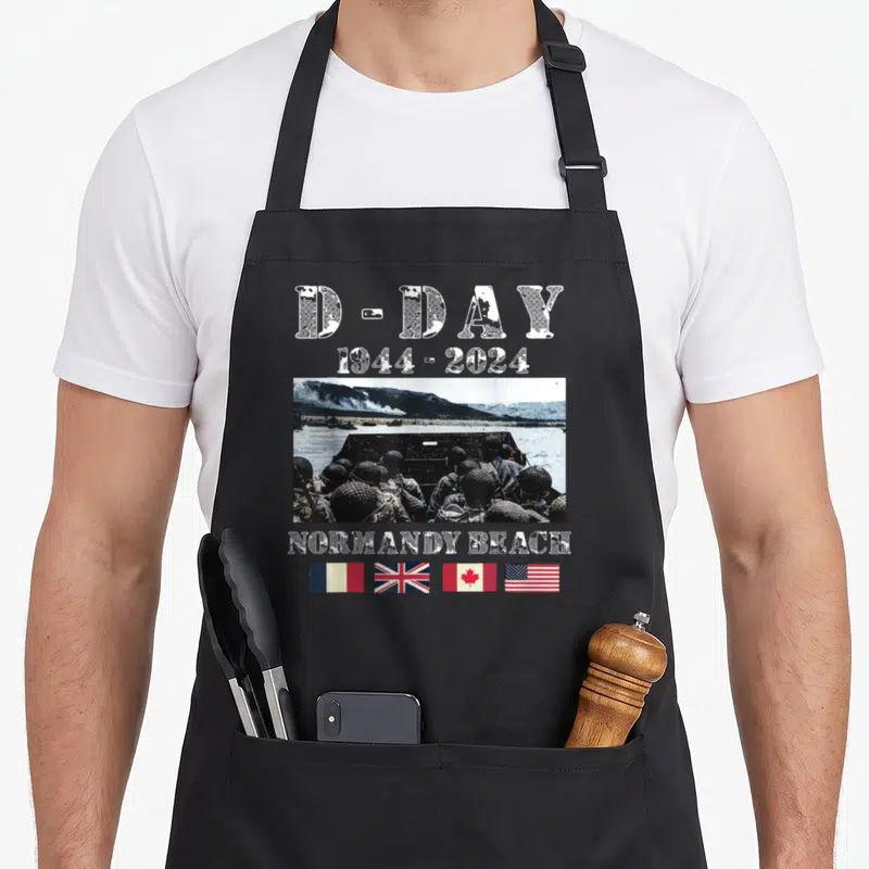 Tablier de cuisine noir avec illustration historique D-Day 1944-2024 et quatre drapeaux nationaux alignés en bas.