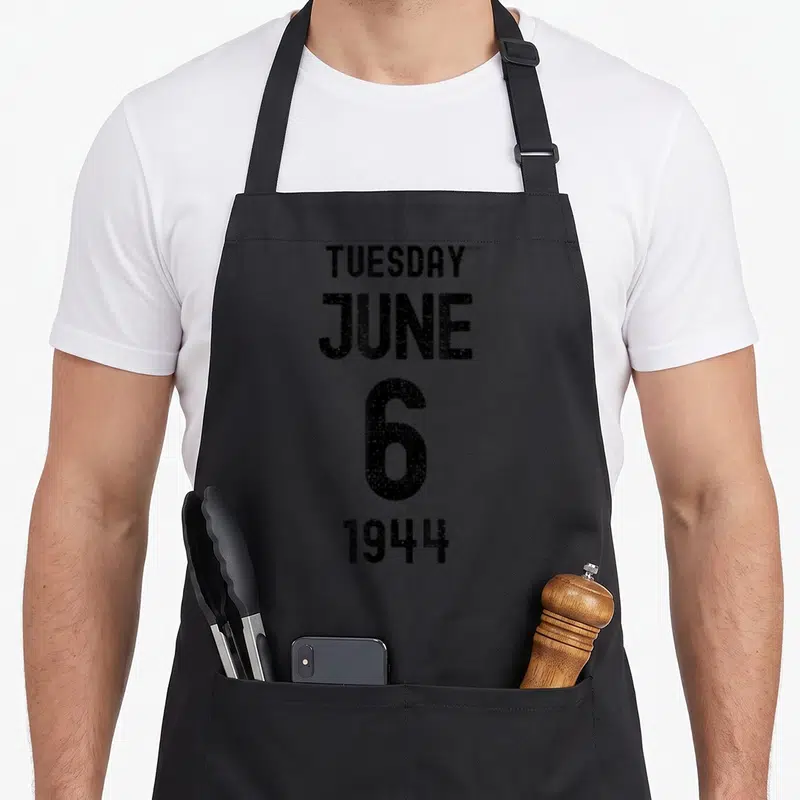Tablier de cuisine noir avec le texte Tuesday June 6 1944 imprimé en noir au centre du devant.