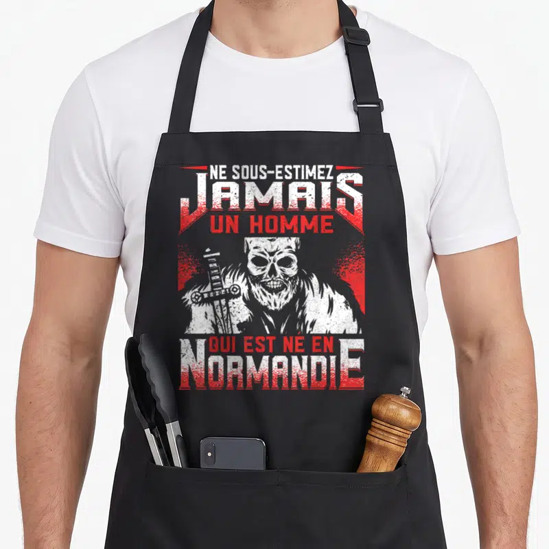Tablier de cuisine noir avec illustration crâne guerrier et texte rouge Ne sous-estimez jamais un homme qui est né en Normandie.