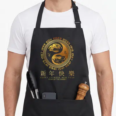 Tablier de cuisine noir avec emblème doré représentant deux lapins dans un cercle zodiacal et des caractères chinois.