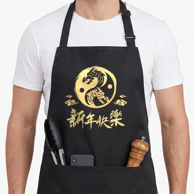Tablier de cuisine noir avec un grand motif circulaire doré représentant un dragon et des nuages asiatiques.