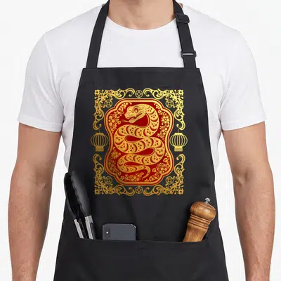 Tablier de cuisine noir avec illustration rouge et dorée d'un serpent enroulé entouré de lanternes et de motifs floraux chinois.