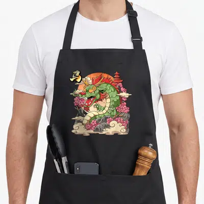 Tablier de cuisine noir avec un dragon vert entouré de fleurs roses, nuages et pagode orange.