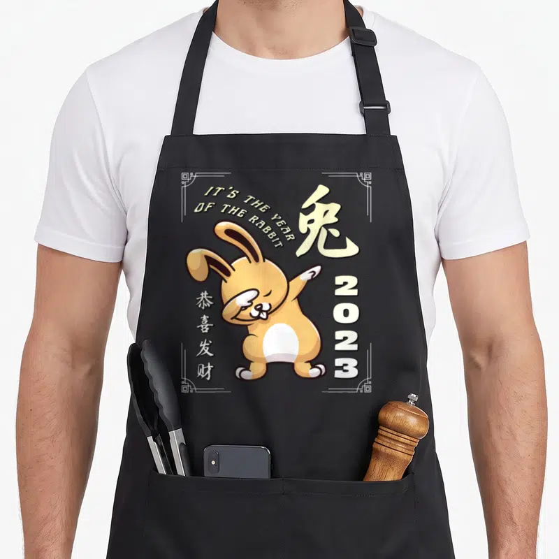 Tablier de cuisine noir avec un lapin orange effectuant un dab et l'année 2023 imprimés en centre.