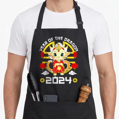 Tablier de cuisine noir avec un dragon mignon en tenue rouge, lanternes et l'inscription YEAR OF THE DRAGON 2024.
