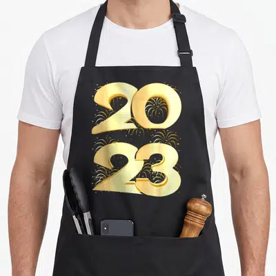 Tablier de cuisine noir avec les chiffres 2023 en or et des motifs de feux d'artifice dorés sur le devant.