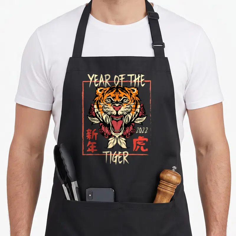 Tablier de cuisine noir avec illustration d'un tigre rugissant encadré de roses et de texte Year of the Tiger 2022.