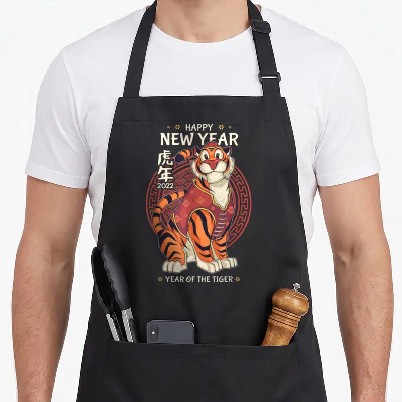 Tablier de cuisine noir avec un tigre cartoon en tenue rouge et les textes Happy New Year 2022.
