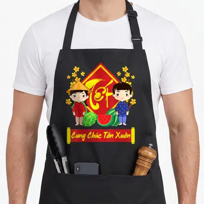 Tablier de cuisine noir avec enfants en Ao Dai, lettrage Têt et fruits festifs rouges et jaunes.