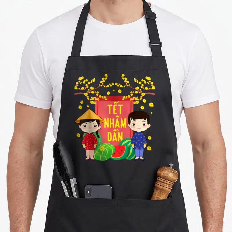 Tablier de cuisine noir avec deux enfants en tenues traditionnelles vietnamiennes et des fleurs jaunes sur fond rouge.