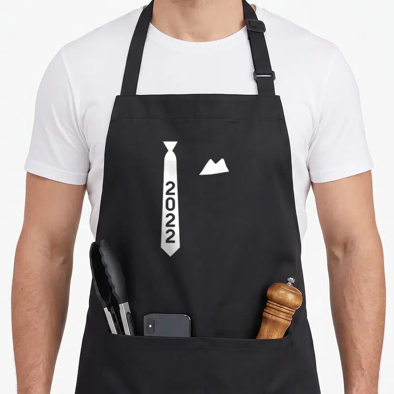 Tablier de cuisine noir avec une illustration de cravate blanche portant l'inscription 2022 et un bout de mouchoir.