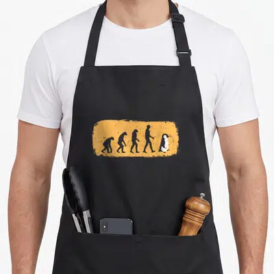 Tablier de cuisine noir avec illustration évolutive menant à un pingouin debout sur fond orange texturé.