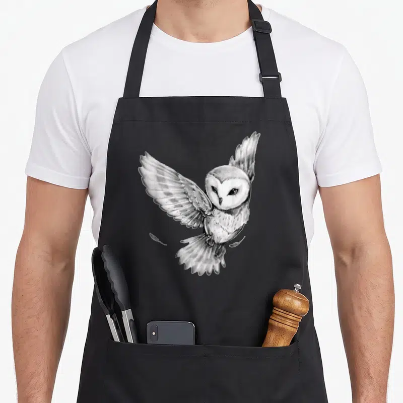 Tablier de cuisine noir avec illustration réaliste d'un hibou aux ailes déployées en noir et blanc.