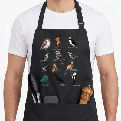 Tablier de cuisine noir avec une planche naturaliste montrant douze espèces d'oiseaux colorés comme le Guêpier d'Europe et le Kookaburra.