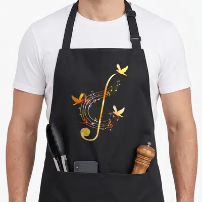 Tablier de cuisine noir avec une illustration colorée d'une clé de sol et d'oiseaux en vol aux teintes orange et jaune.