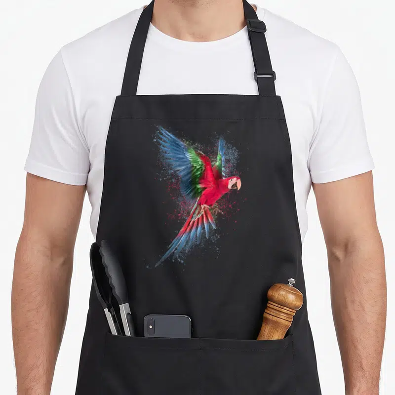Tablier de cuisine noir avec un perroquet aux ailes déployées et des éclats de couleurs vives.