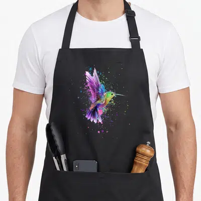 Tablier de cuisine noir avec un colibri multicolore en aquarelle et des éclaboussures de peinture.