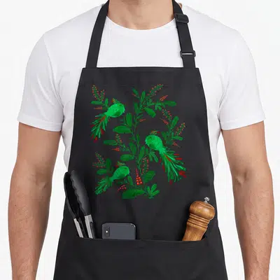 Tablier de cuisine noir avec deux oiseaux verts et des plantes rouges et vertes en motif floral.
